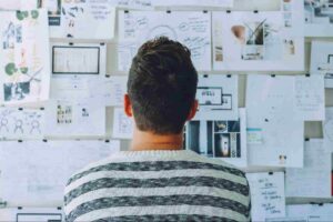 man staring at papers on the wall to solve a problem