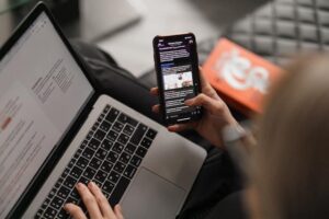 Young caucasian woman on leather couch working at a laptop while browsing her phone
