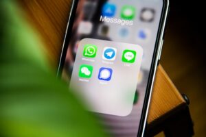 Close-up of a smartphone screen displaying a "Messages" folder containing icons for WhatsApp, Telegram, LINE, WeChat, and Signal.