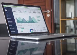 An open laptop sitting on a reflective desk displaying a detailed web-based analytics dashboard.